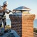 Technician wearing a safety harness inspects a masonry chimney with a stainless steel cap showing light rust and salt residue on a Florida coastal rooftop, with the ocean and palm trees softly blurred in the background at golden hour.