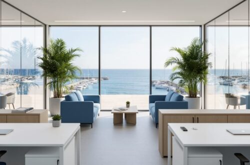 Staged coastal commercial office with white desks, soft blue chairs, light wood accents, glass partitions, and potted palms, lit by soft daylight, with floor-to-ceiling windows revealing a slightly blurred marina and terrace outside.