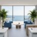 Staged coastal commercial office with white desks, soft blue chairs, light wood accents, glass partitions, and potted palms, lit by soft daylight, with floor-to-ceiling windows revealing a slightly blurred marina and terrace outside.