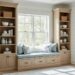 Southern-coastal nook with a built-in window seat with storage and floor-to-ceiling shiplap bookcases, sunlit from the side, with a softly blurred kitchen banquette and mudroom bench in the background.