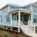 “Modern coastal home with elevated foundation, covered porch, and large windows facing the ocean under soft overcast light.”