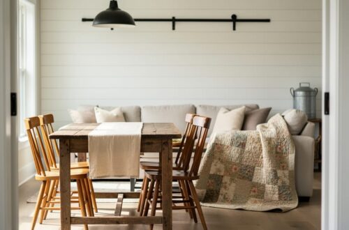 Cozy living room with weathered wood farmhouse table, patchwork quilt, white shiplap wall, and black metal accents in soft natural light.
