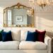 Glamorous Southern living room with a creamy linen sofa, velvet pillows, gold-rimmed mirror, and crystal chandelier reflecting warm sunlight.