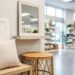 Coastal and farmhouse home décor items on display in a bright showroom, including a whitewashed wall piece, textured throw pillow, rattan accent table, and a decorative mirror.
