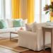 Summer-styled coastal living room with linen pillows, sea-glass green accents, a jute rug, and a vase of magnolia branches and wildflowers in natural daylight.