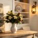A warm-lit antique brass lantern and ironstone pitcher with magnolia branches styled on a patinaed farmhouse table against white shiplap, with linen curtains and a weathered wooden sign in view.