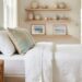 Sunlit coastal-style living room vignette featuring white linen bedding, a rattan side table, and an organic ceramic vase in muted sea-glass and sand tones.