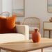 “Burnt orange velvet pillow and terracotta decor styled on a cream sofa in a bright coastal-inspired living room with soft golden light.”