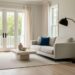 Sunlit modern coastal living room with neutral upholstery, a bold accent pillow, and a sculptural floor lamp in an uncluttered open layout.