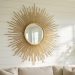 Gold sunburst mirror with radiating metal rays mounted on a whitewashed wall in a bright Southern coastal living room.