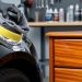Close-up of a buffing pad and microfiber cloth polishing a glossy car fender next to a lacquered wooden drawer in a workshop setting.