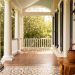 Sunlit Southern porch and interior with white columns, wrought-iron decor, indigo textiles, and a sweetgrass basket on a cypress table, suggesting diverse regional craftsmanship.